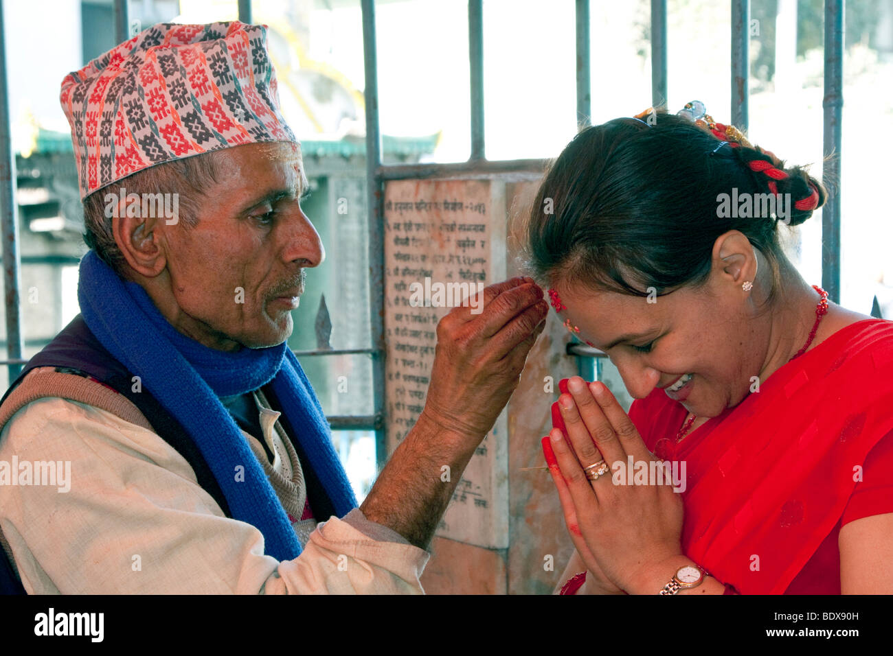 Kathmandu, Nepal.  A Hindu Priest Blesses a Worshiper by Applying a Tika of Rice and Sindur Powder to the Forehead. Stock Photo