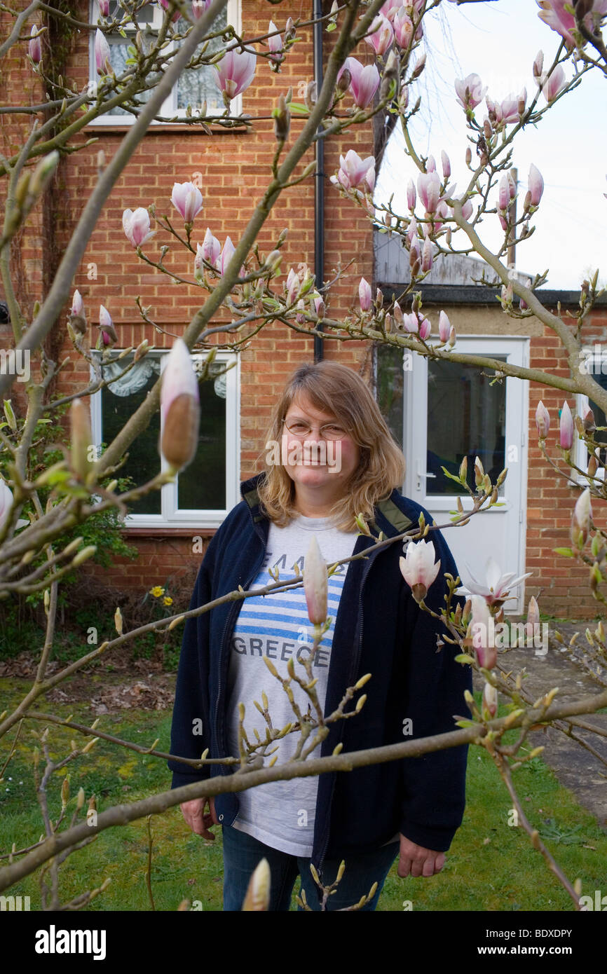 A middle aged woman in her 50's stands behind a tree in her garden at her home in Sevenoaks. Stock Photo