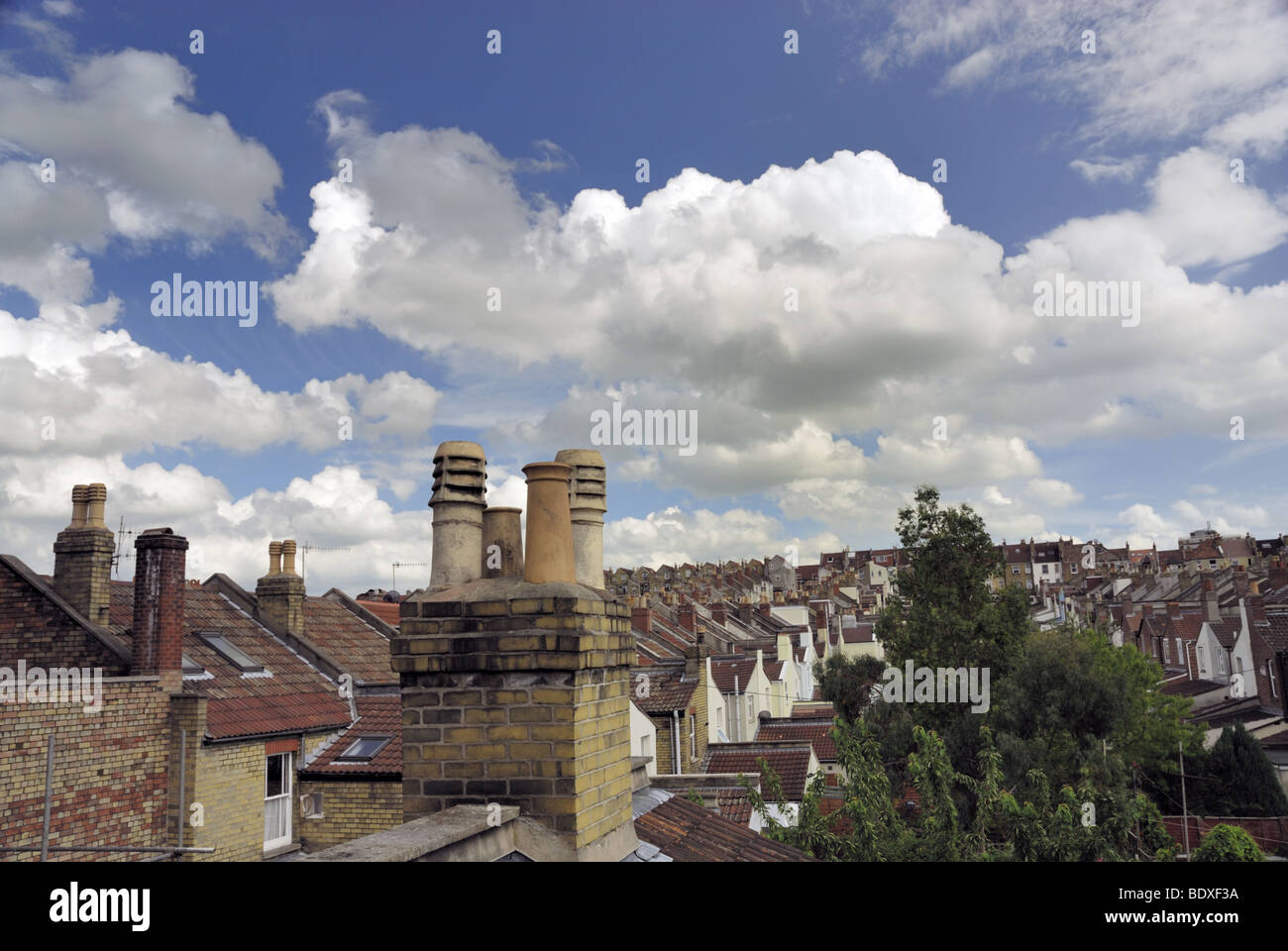Rooftop view of Terraced housing and chimney pots with a blue sky and fluffy white clouds. Stock Photo