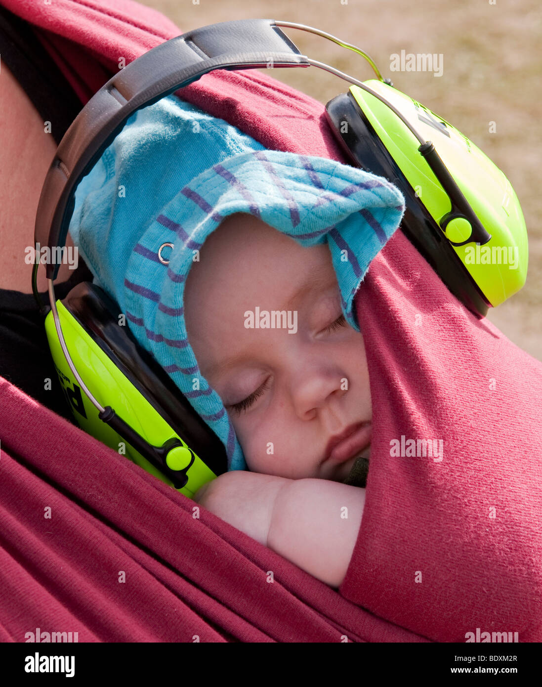 A peacefully sleeping baby at a music festival, wearing ear defenders