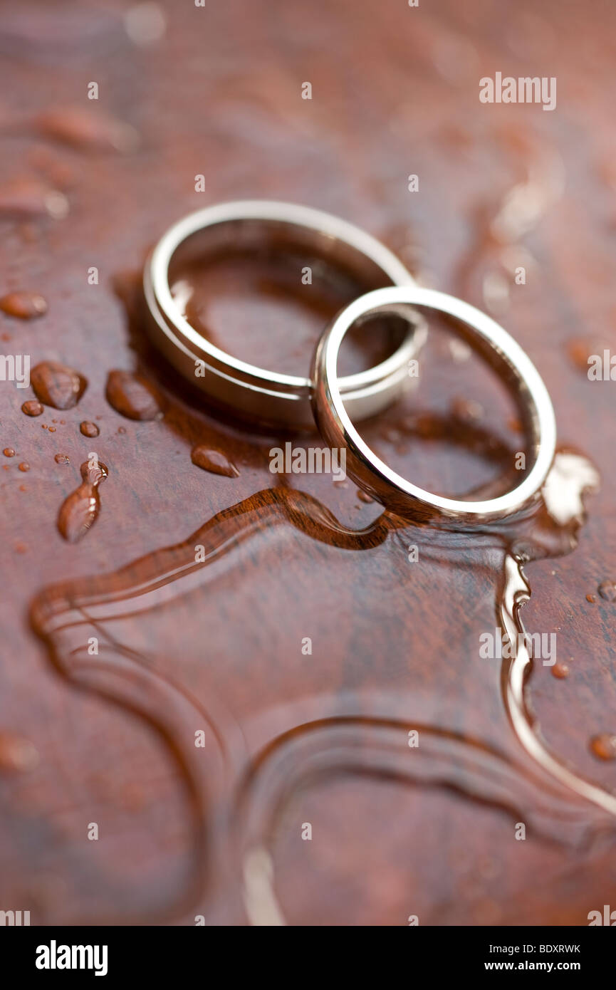 A pair of gold wedding rings on a wet polished wood surface Stock Photo