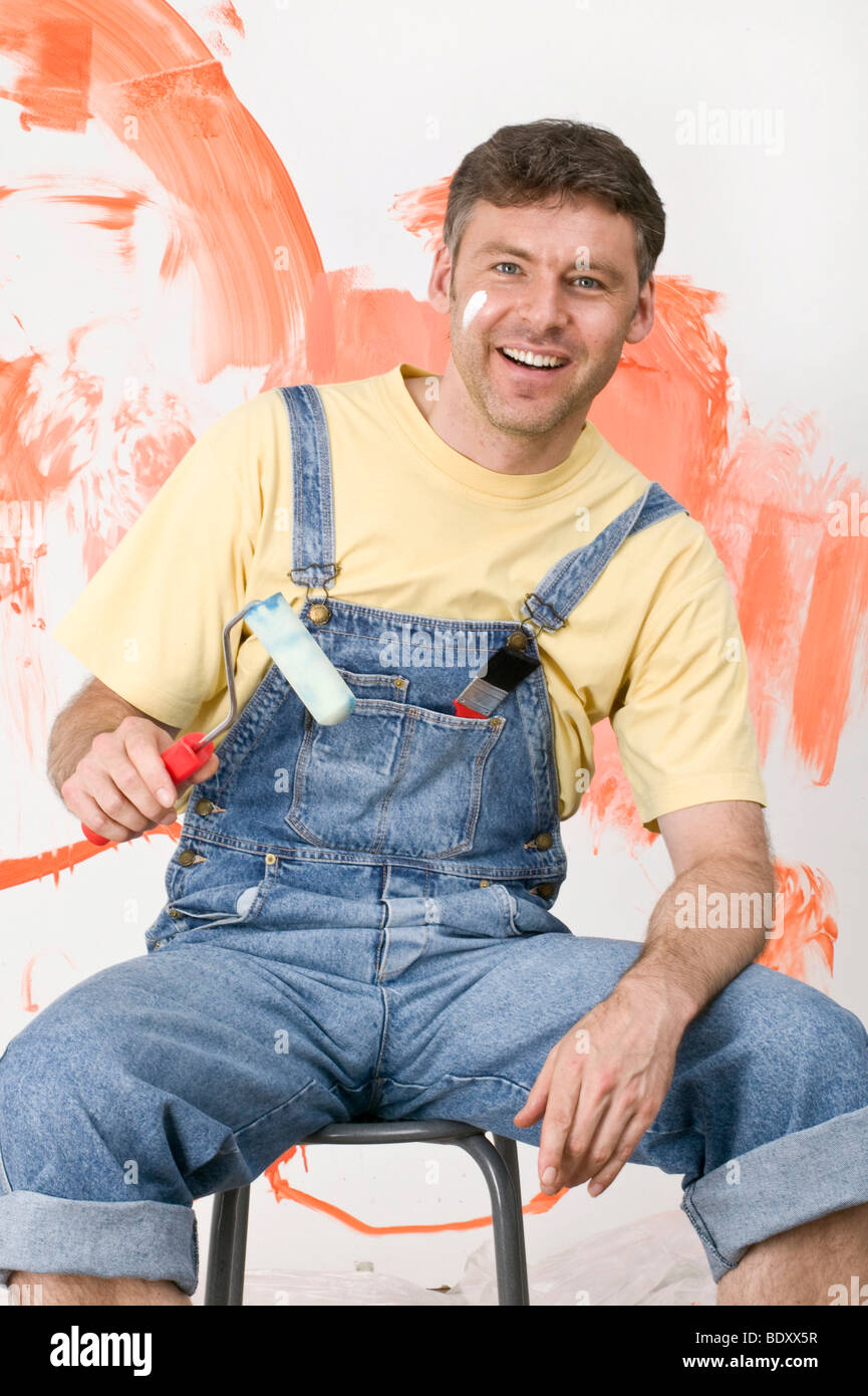 Young man in dungarees with painting utensils Stock Photo