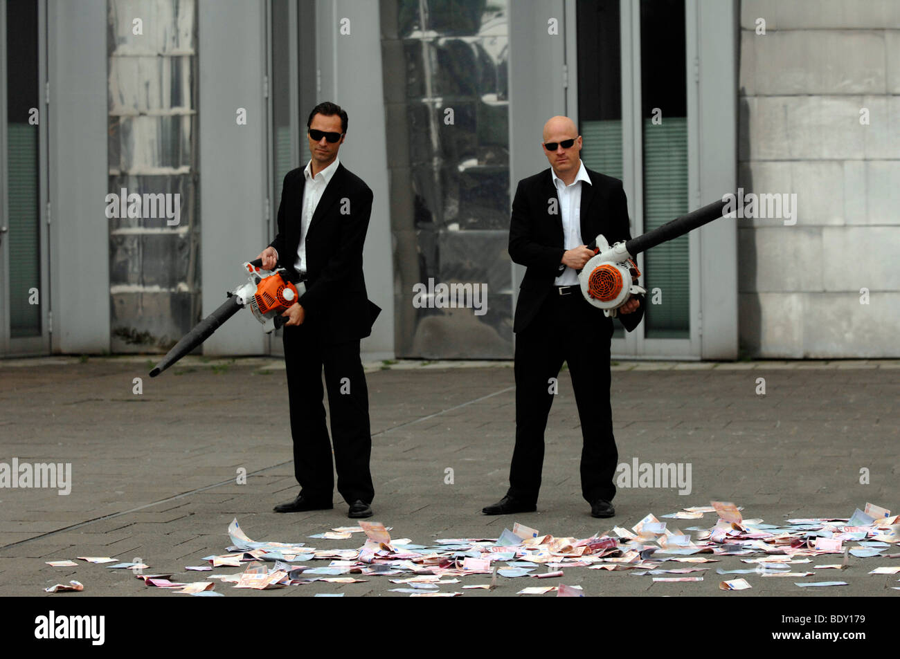 Men in Black, two business people with leaf blowers and banknotes, symbolic of waste of money Stock Photo