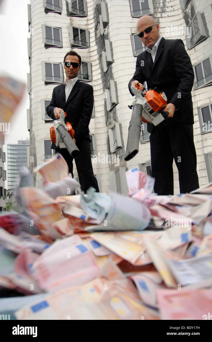 Men in Black, two business people with leaf blowers and banknotes, symbolic of waste of money Stock Photo