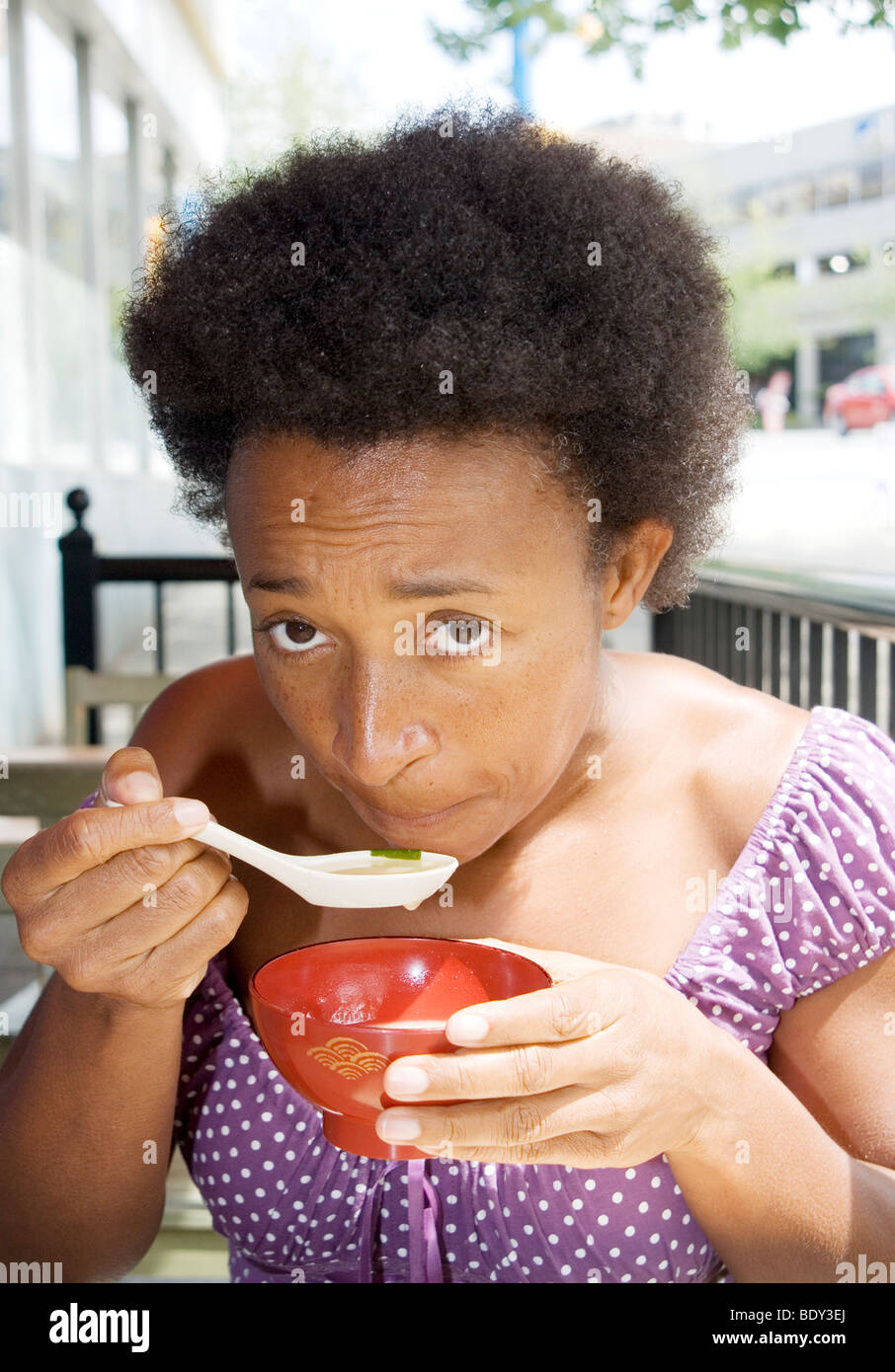 African American woman eating miso soup in outdoor cafe, Vancouver Stock Photo