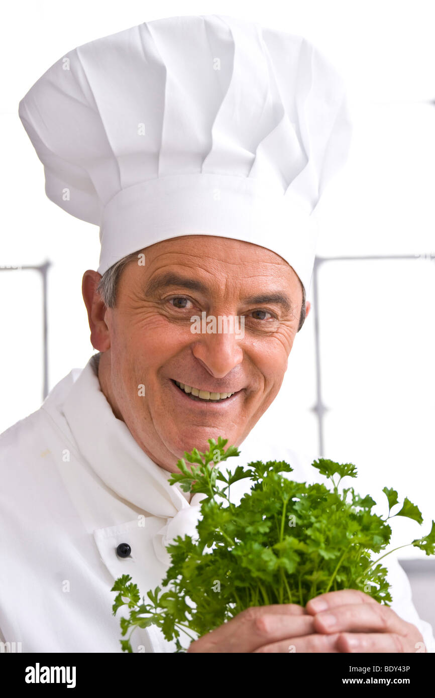 Chef wearing a chef's hat holding a bunch of parsley in his hand Stock Photo
