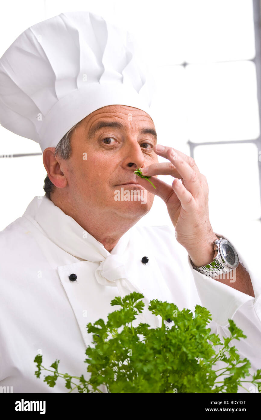 Chef wearing a chef's hat smelling parsley Stock Photo