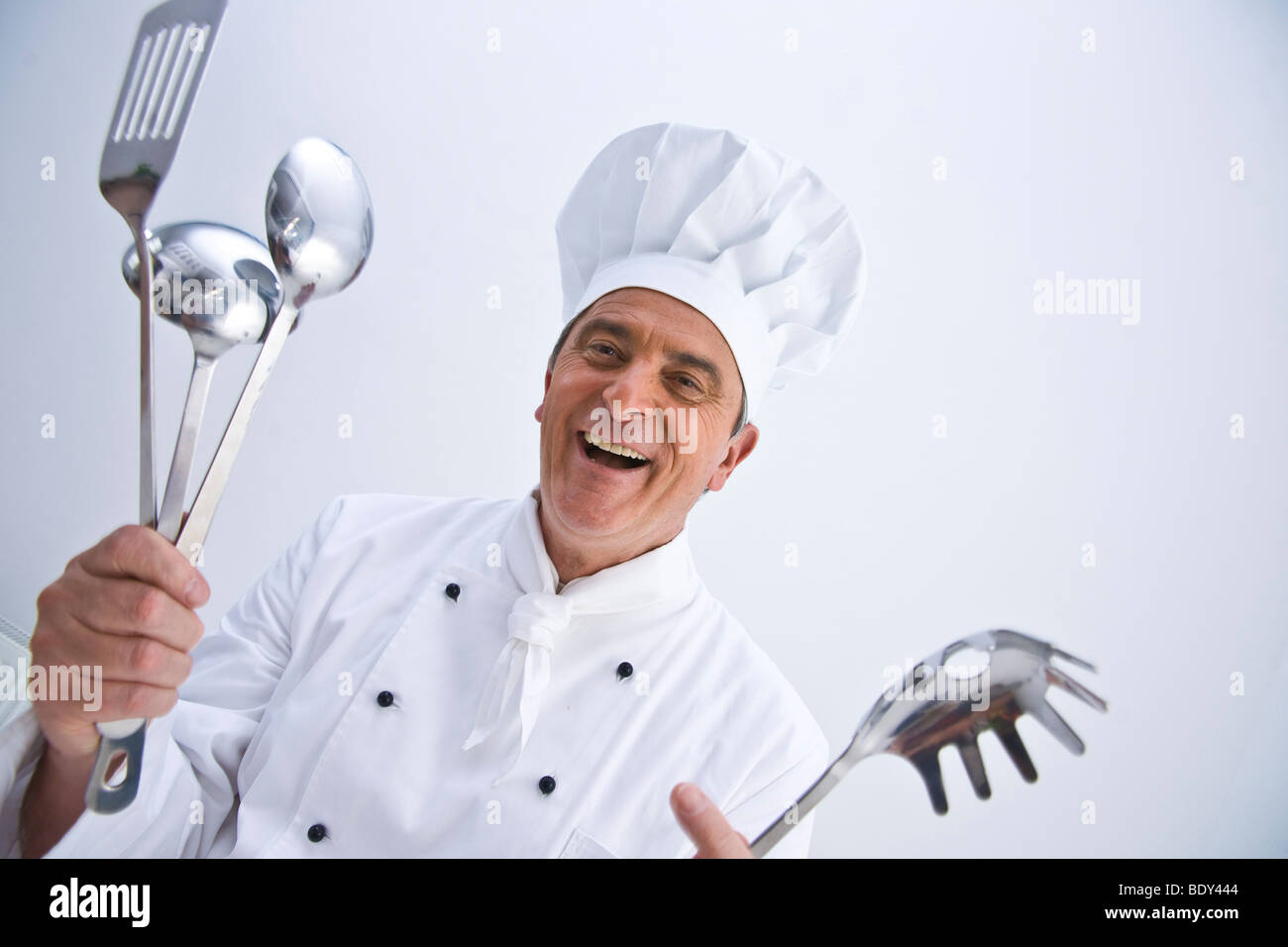 Chef wearing a chef's hat holding cooking utensils in his hands Stock