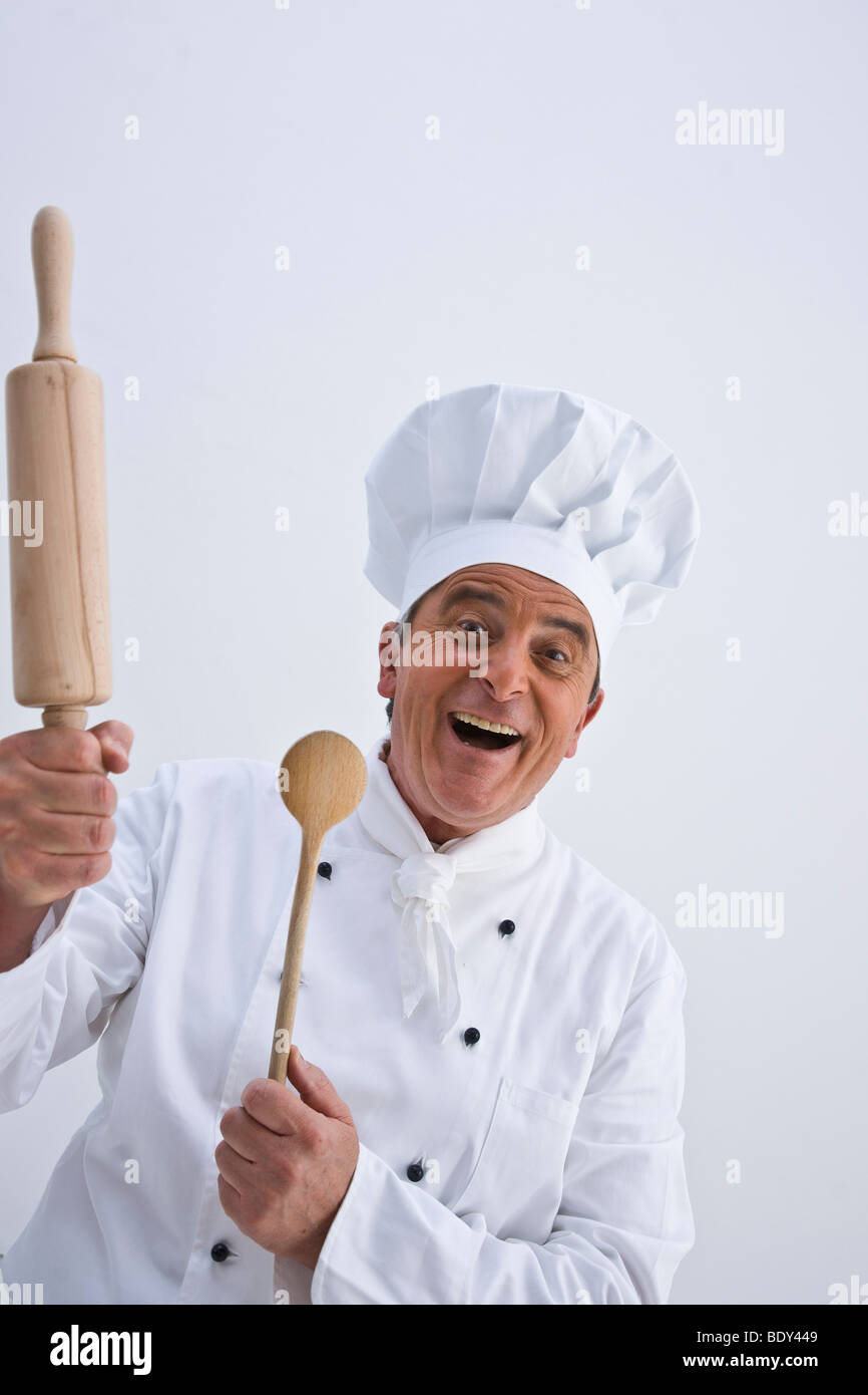 Chef wearing a chef's hat holding a wooden spoon and a rolling pin in