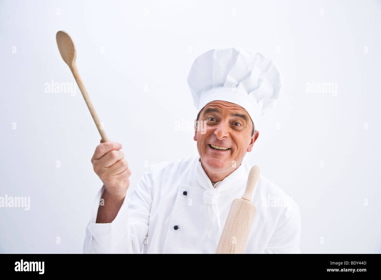Chef wearing a chef's hat holding a wooden spoon and a rolling pin in