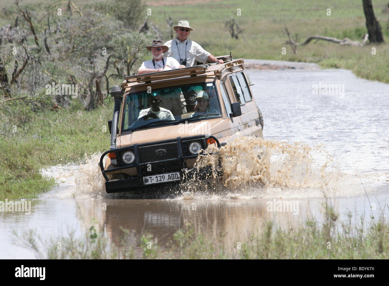 Africa, Tanzania, Serengeti National Park, Safari tourists in an open top Jeep crossing a water barrier Stock Photo