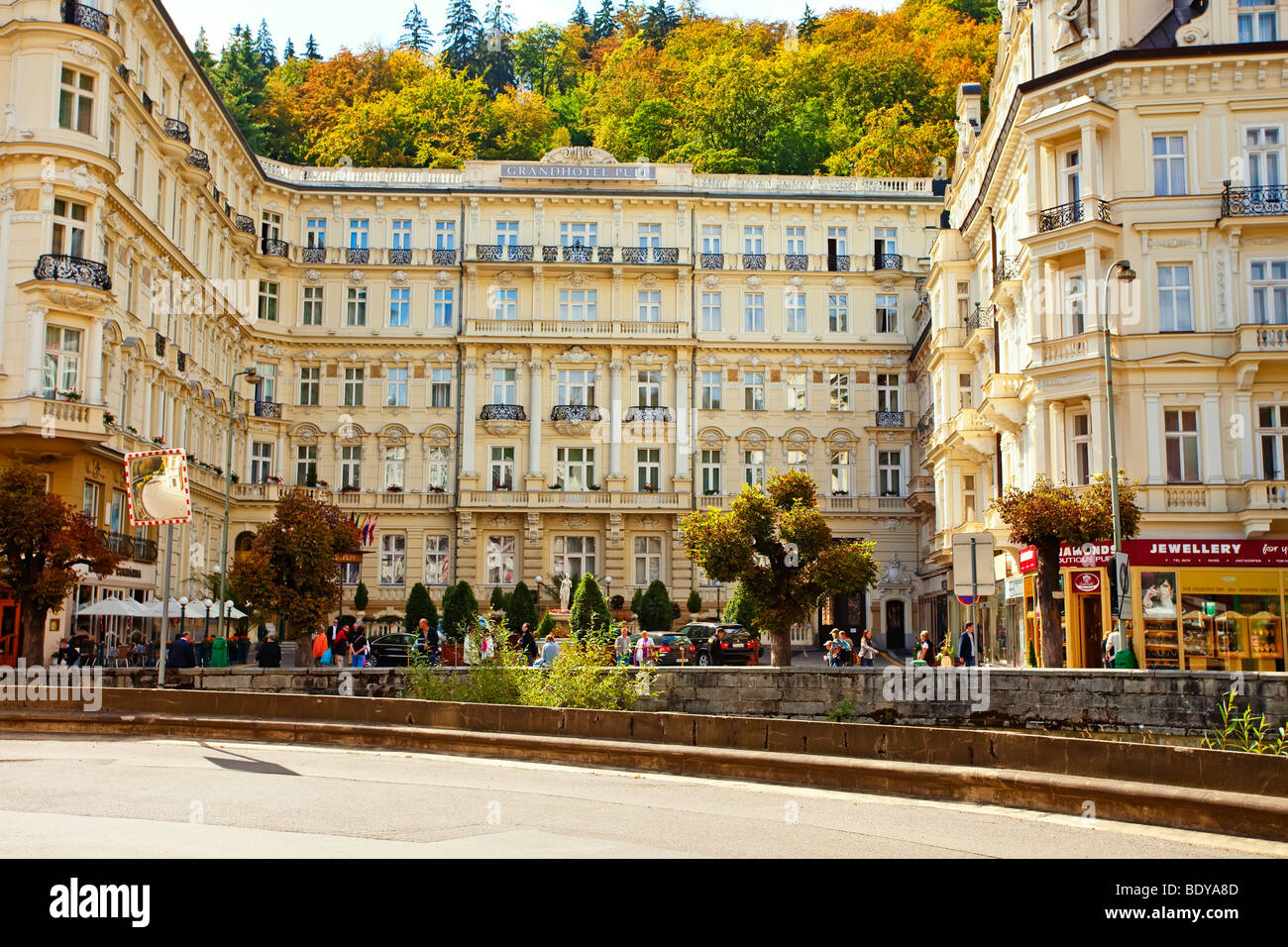 Elegant Grandhotel Pupp in Karlovy Vary with ornate historic facade, autumn trees, shops, and people walking in front of the spa town square Stock Photo