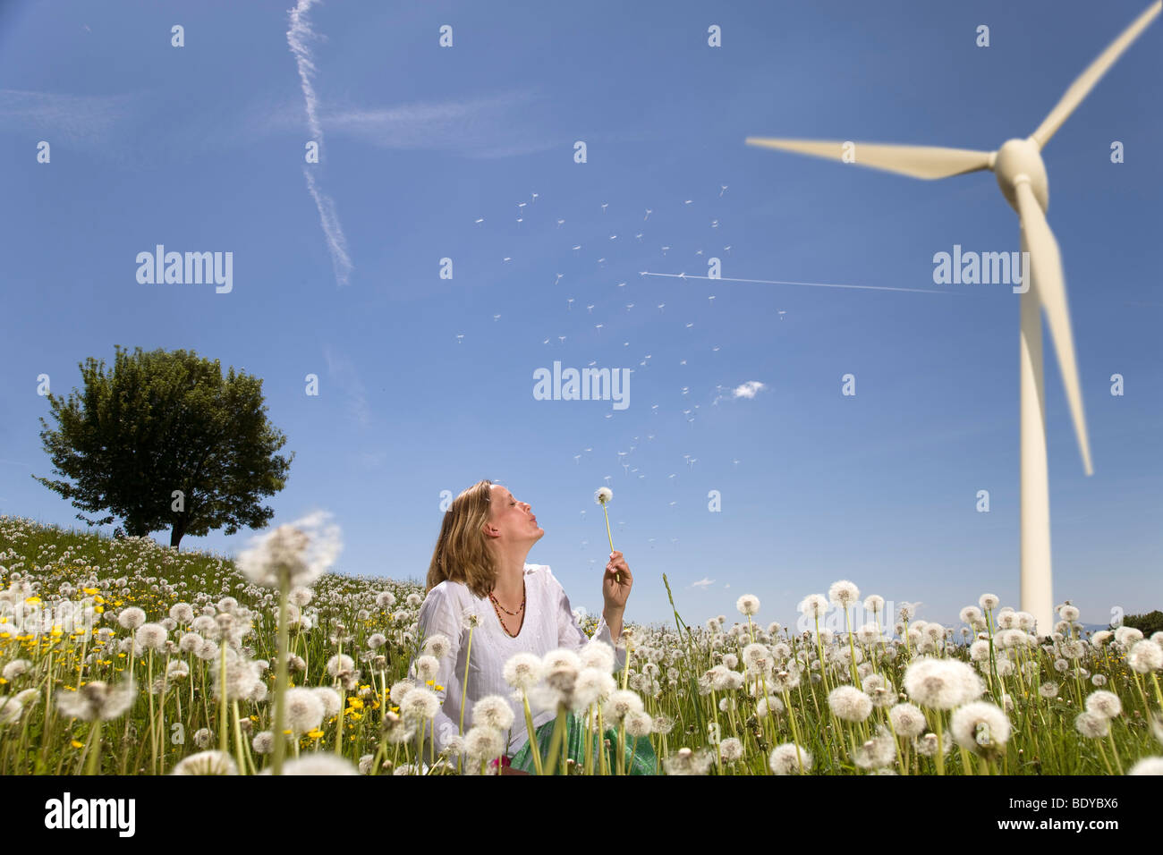 woman blowing dandelion at wind turbine Stock Photo