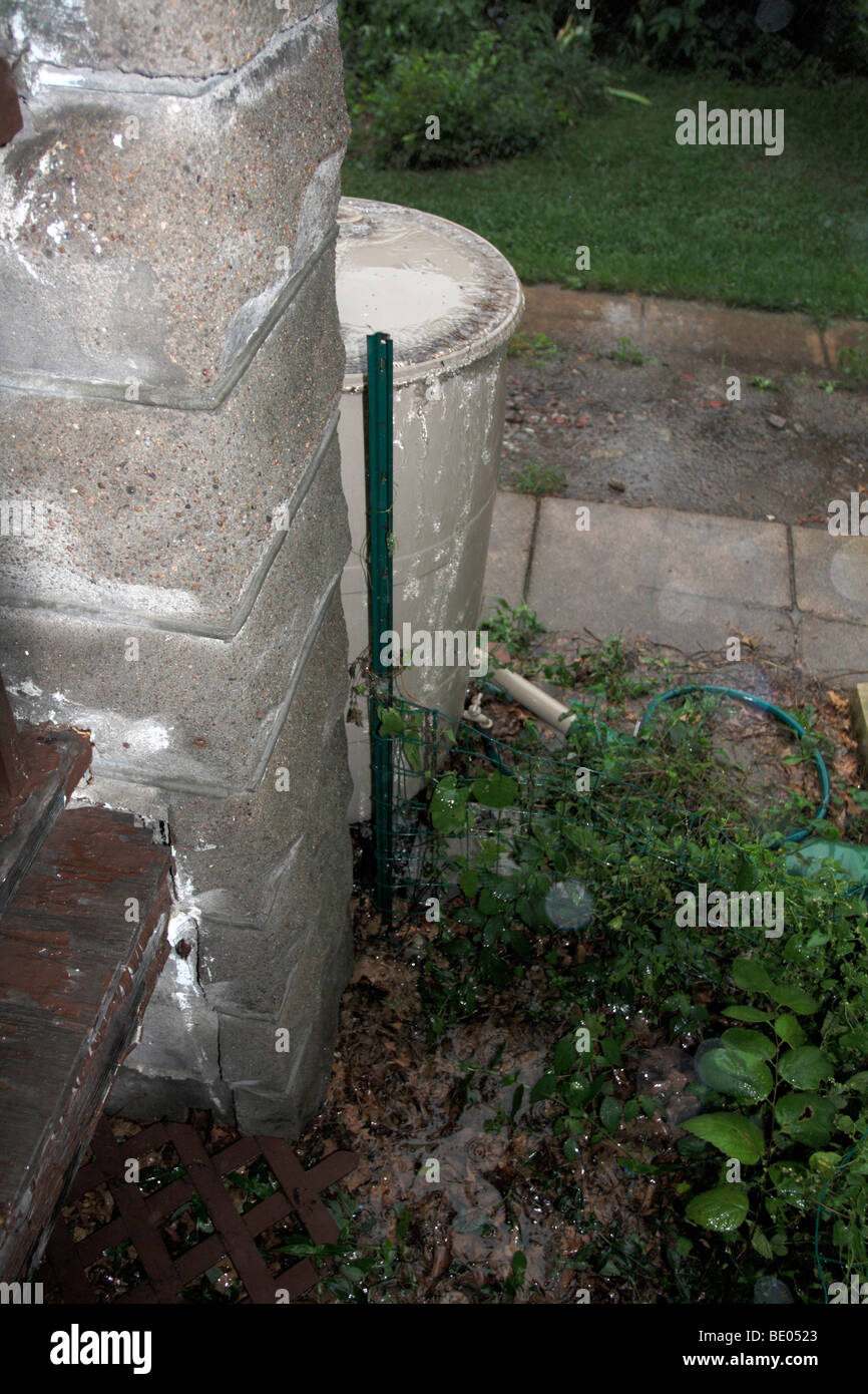 Overflowing homemade rain barrel near concrete column. Stock Photo