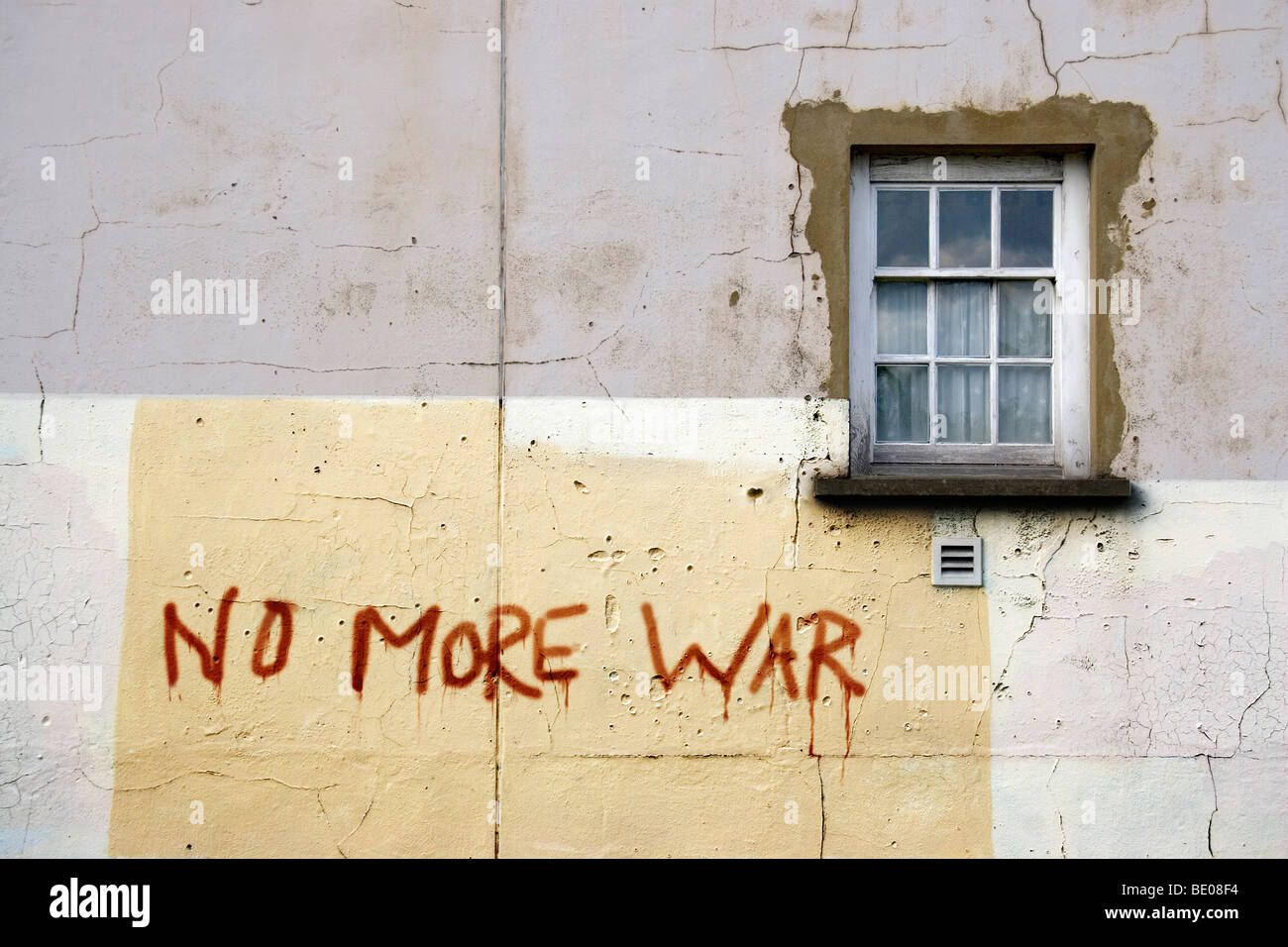 Bullet damaged wall of a building with a window and graffiti reading 'no more war'. Stock Photo