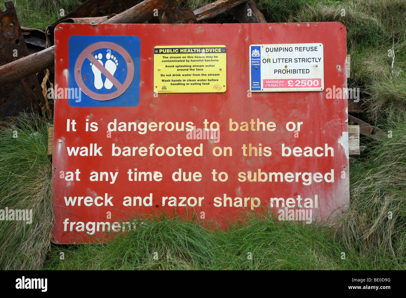 A sign on a beach saying it is dangerous to bathe or walk barefoot because of a submerged wreck and sharp metal fragments Stock Photo
