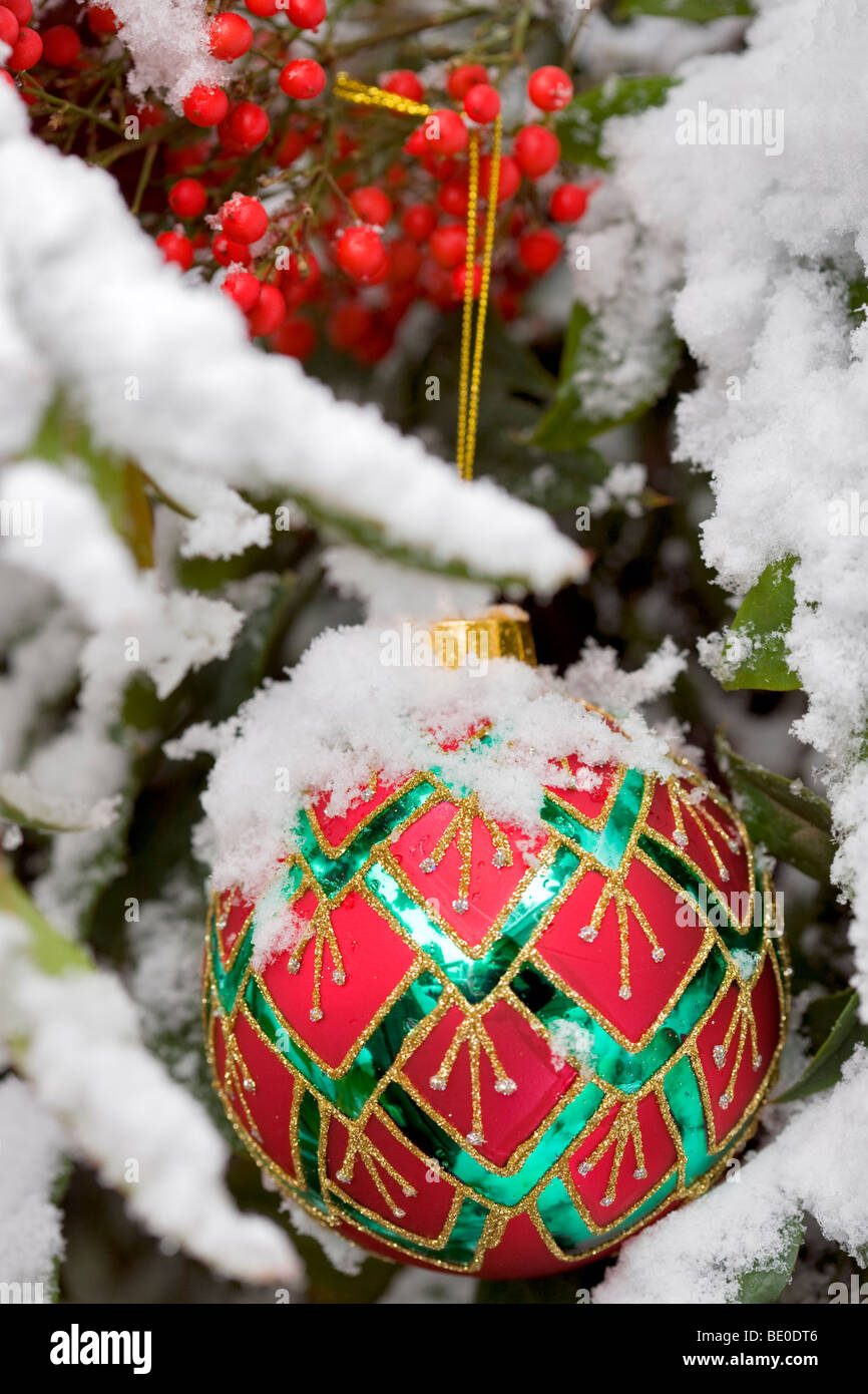 Christmas tree ornament in snow covered bush with red berries. Stock Photo