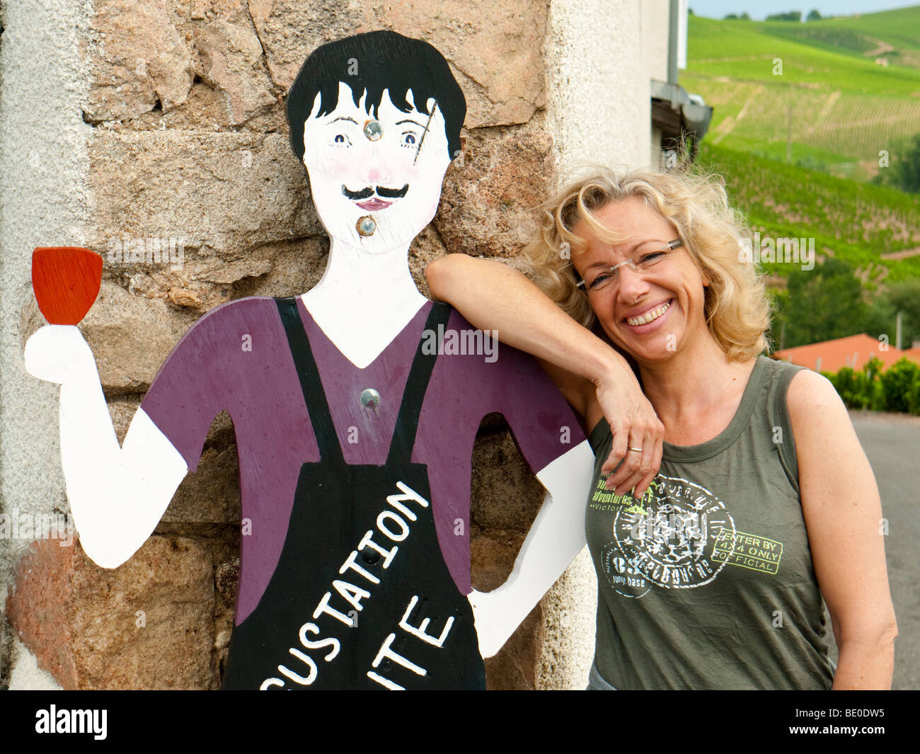 A tourist leans on a wooden figure which resembles a vintner and advertises the renowned Beaujolais wine of Fleurie. Stock Photo