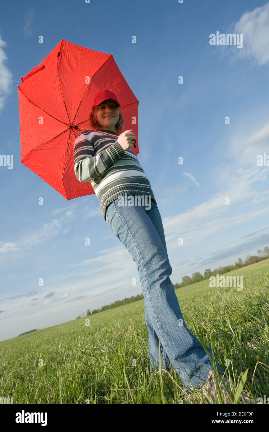 young woman standing under red umbrella on green grass meadow Stock Photo