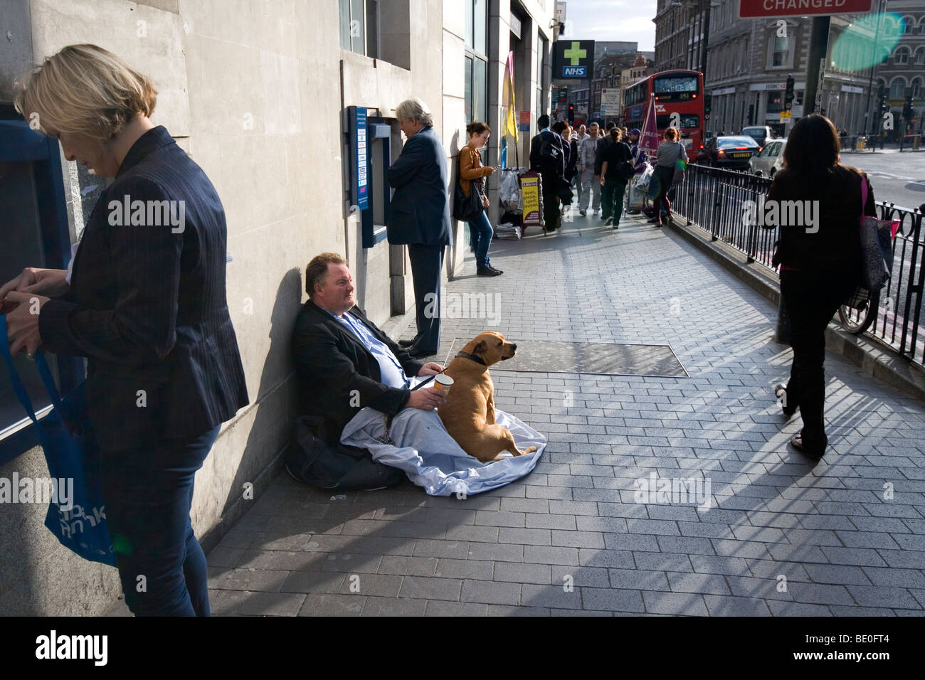 A street beggar strategically seated between two ATM machines in Borough High St, London, SE1 Stock Photo