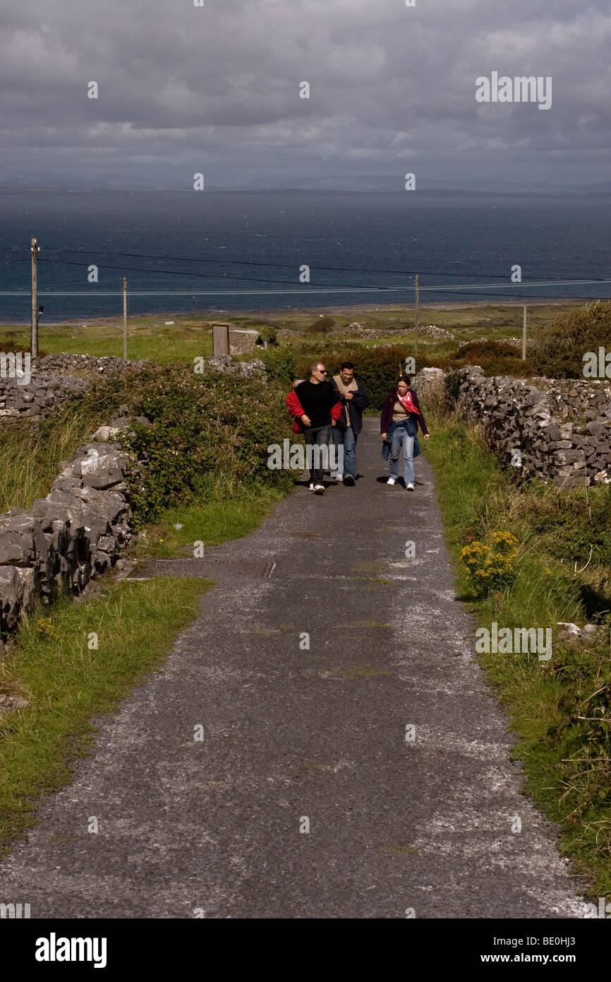 Tourists Walking on a Small Country Road Lined with Traditional Stone Walls, Inis Mor ( Inismore ) Island, Co. Galway, Ireland Stock Photo