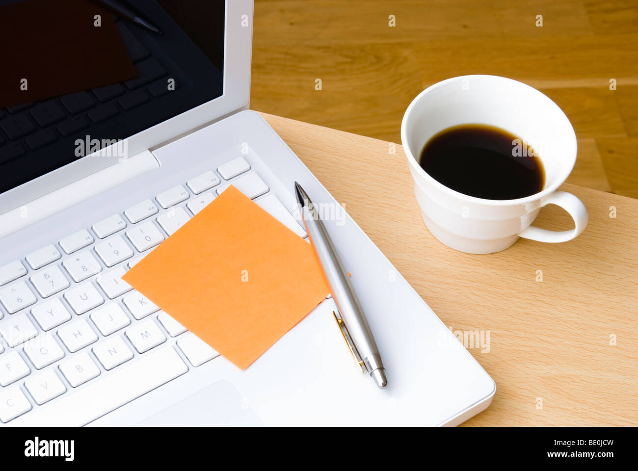 Blank orange postit note on white laptop keyboard with pen and cup of coffee Stock Photo