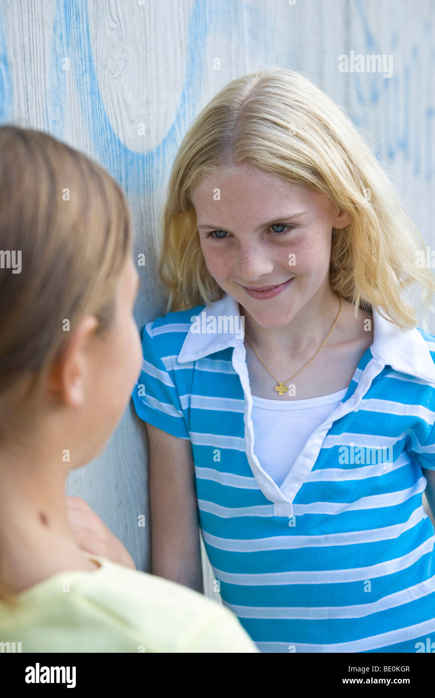Two girls leaning against a wall, talking Stock Photo - Alamy