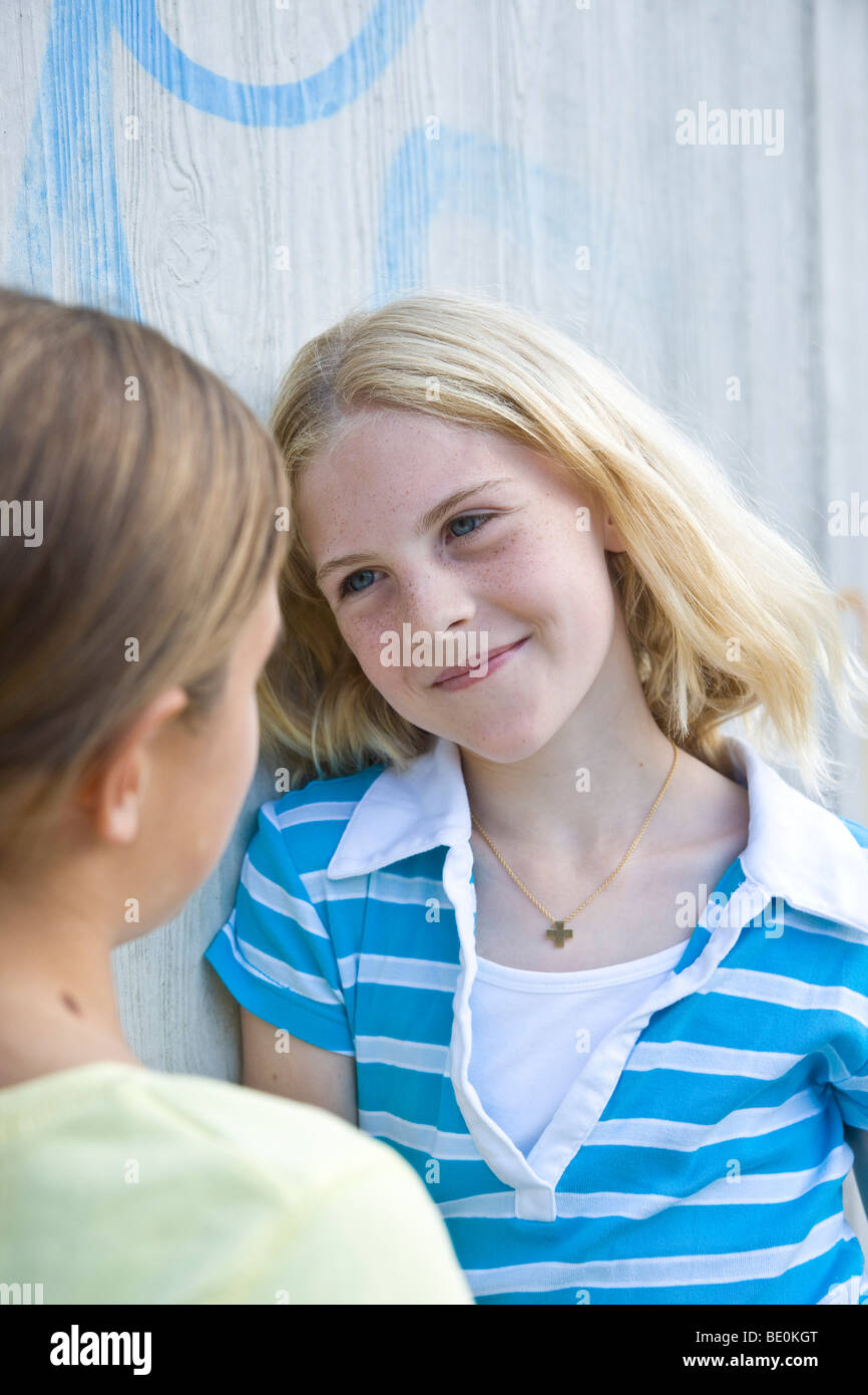 Two girls leaning against a wall, talking Stock Photo - Alamy