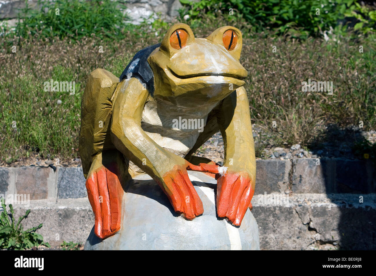 A wooden bullfrog chainsaw carving. He is painted green with orange feet and eyes. Stock Photo