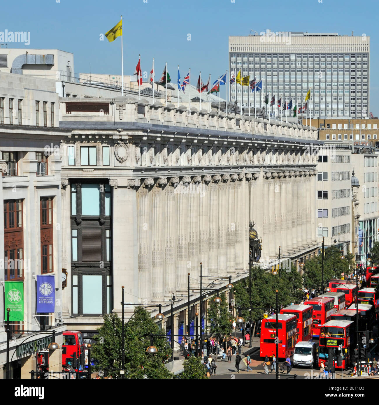 Oxford Street frontage of Selfridges department store with flags flying at roof top level & red London buses West End London England UK Stock Photo