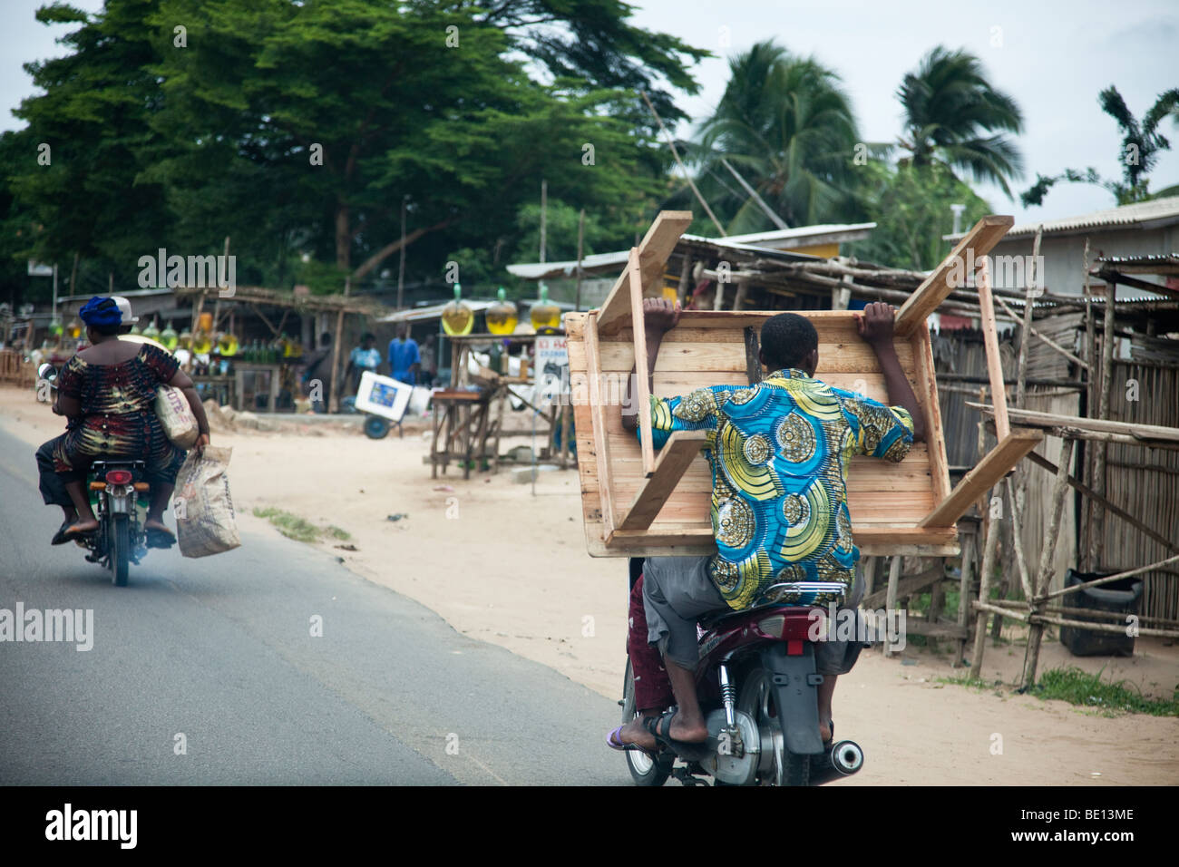 Whizzing through Cotonou, Benin, a man carries a wood table on a motorcycle. Stock Photo