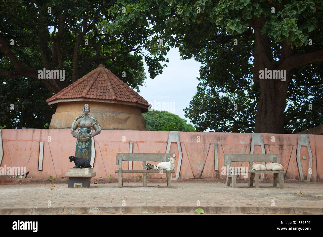 Outside the Temple of Pythons in Oudiah, Benin, a goat sits at the foot of a statue of a woman with a python. Stock Photo