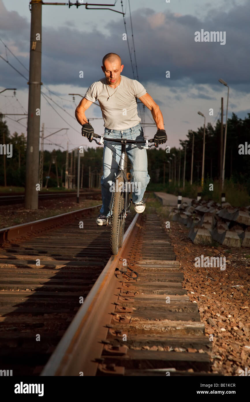 Young man riding with bicycle on railways rail. Stock Photo