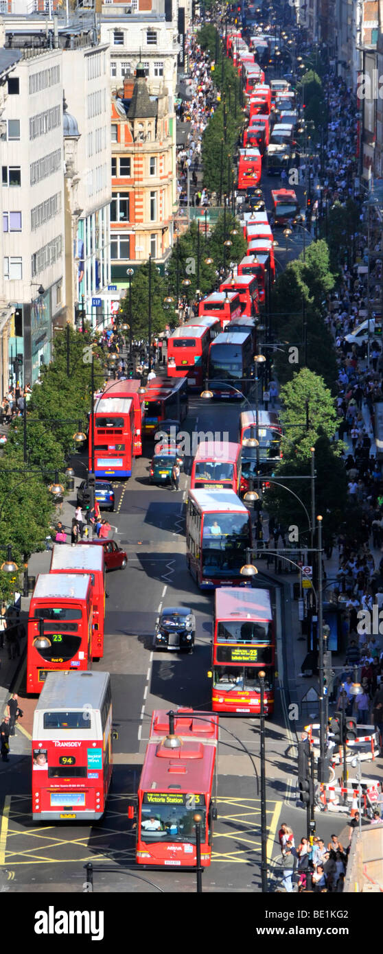 Looking down on UK London Oxford Street with shoppers & aerial views of long queues of double decker red London buses at bus stops & traffic lights Stock Photo