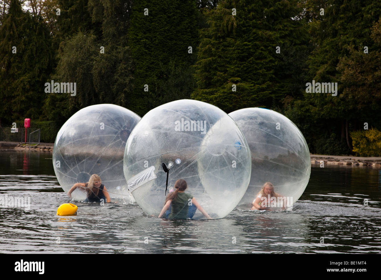 Three young girls playing inside a bubblerunner across the public lake at Rouken Glen park, Glasgow, UK, Scotland Stock Photo