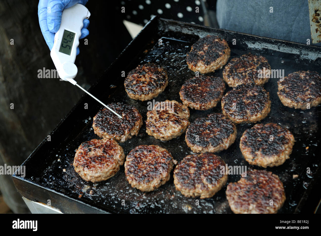 Hamburgers being cooked on hotplate and digital thermometer checking internal temperature Stock Photo