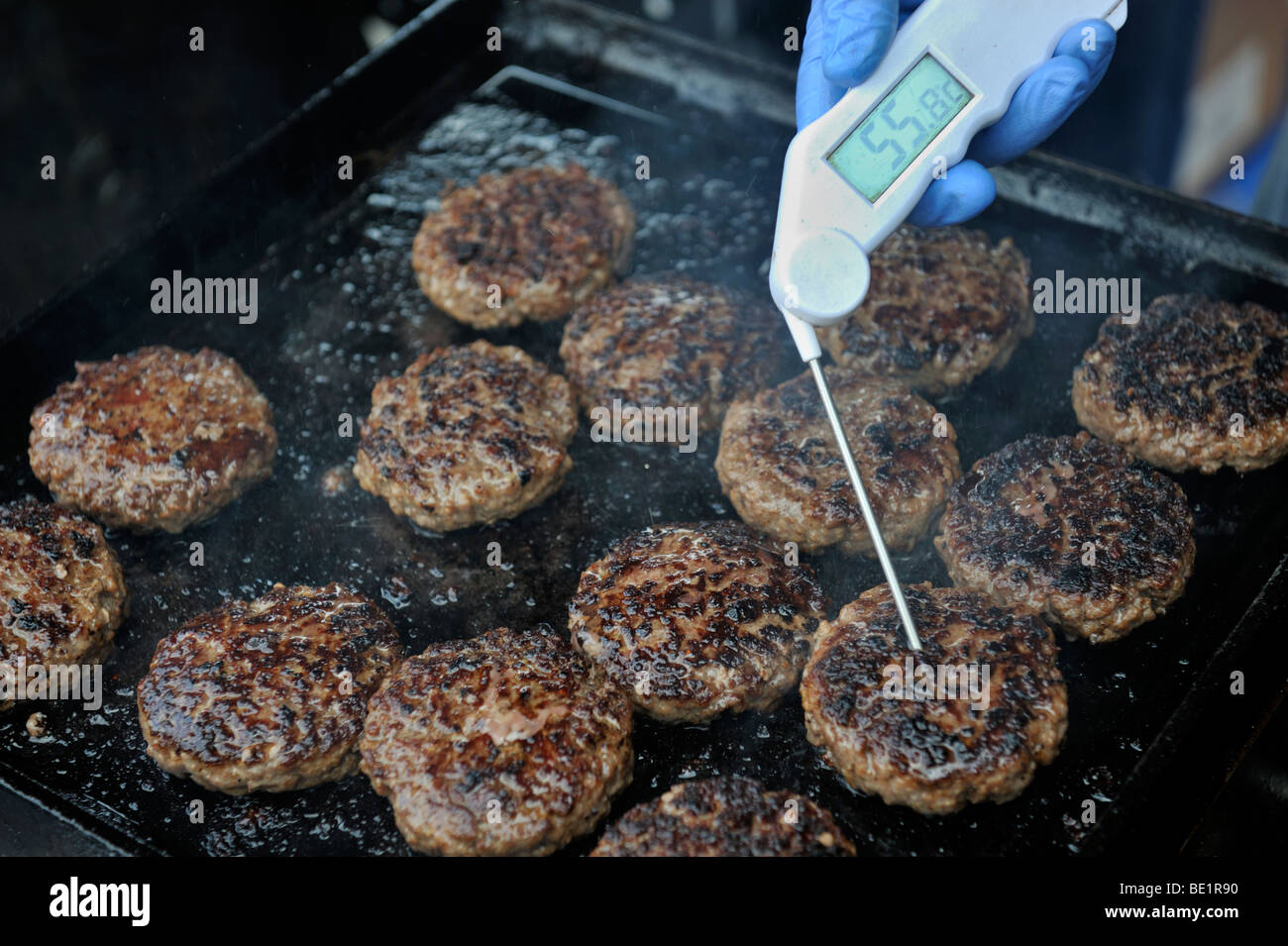 Hamburgers being cooked on hotplate and digital thermometer checking internal temperature Stock Photo