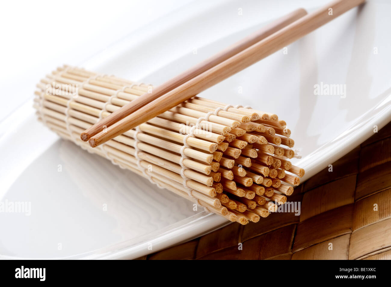 a tilted horizontal macro of a pair of chopsticks and a sushi rolling mat on a white plate Stock Photo