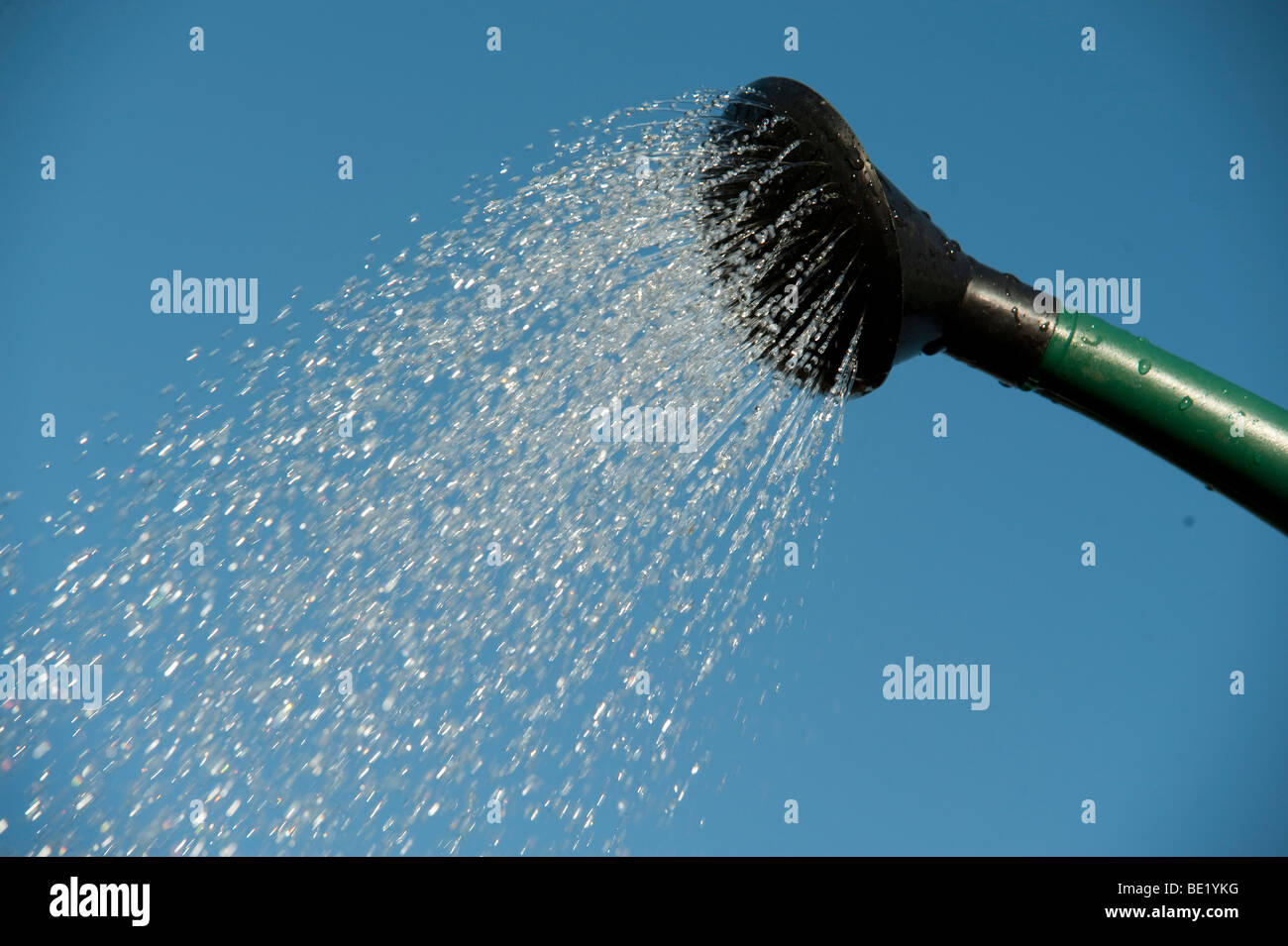 Water pouring from watering can spout against blue sky background sprinkling gardening tool Stock Photo