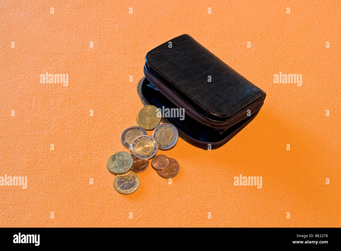 Half-open black leather purse with loose change spread out on an orange support. Porte-monnaie noir et menue monnaie. Stock Photo