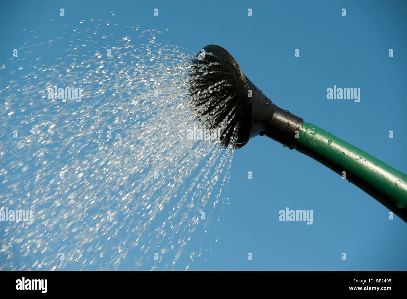 Water pouring from watering can spout against blue sky background sprinkling gardening tool Stock Photo