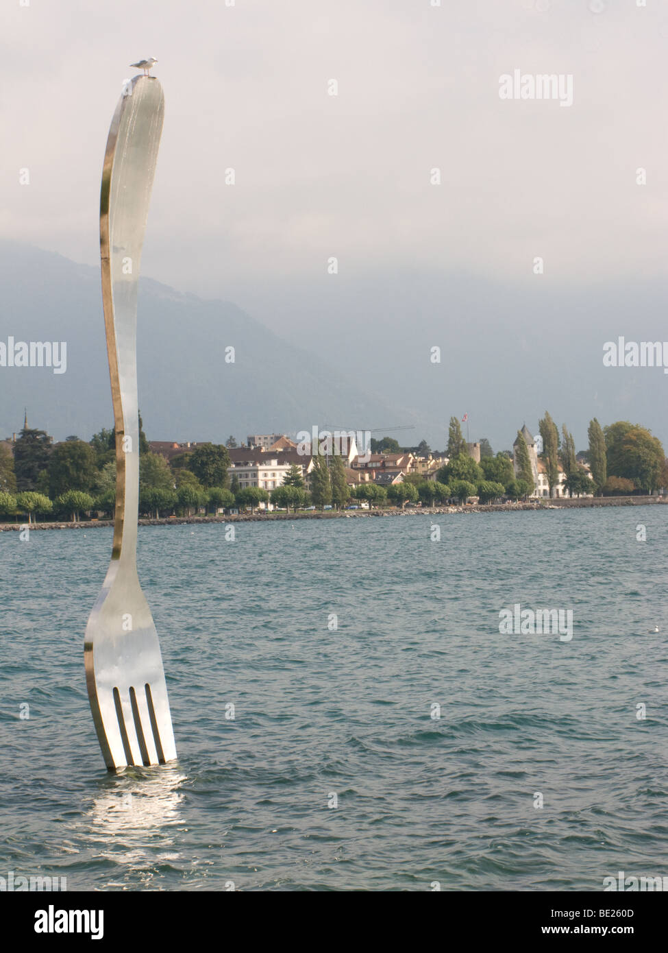 Giant sculptured fork protruding from a lake with a small bird sat on top Stock Photo