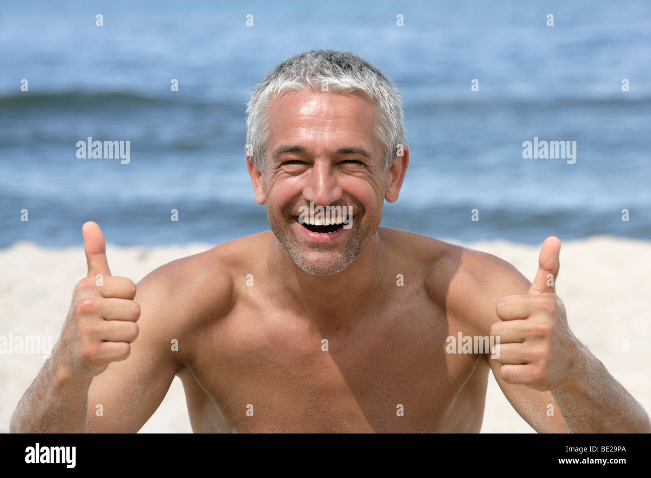 Handsome happy man giving thumbs up on the beach Stock Photo