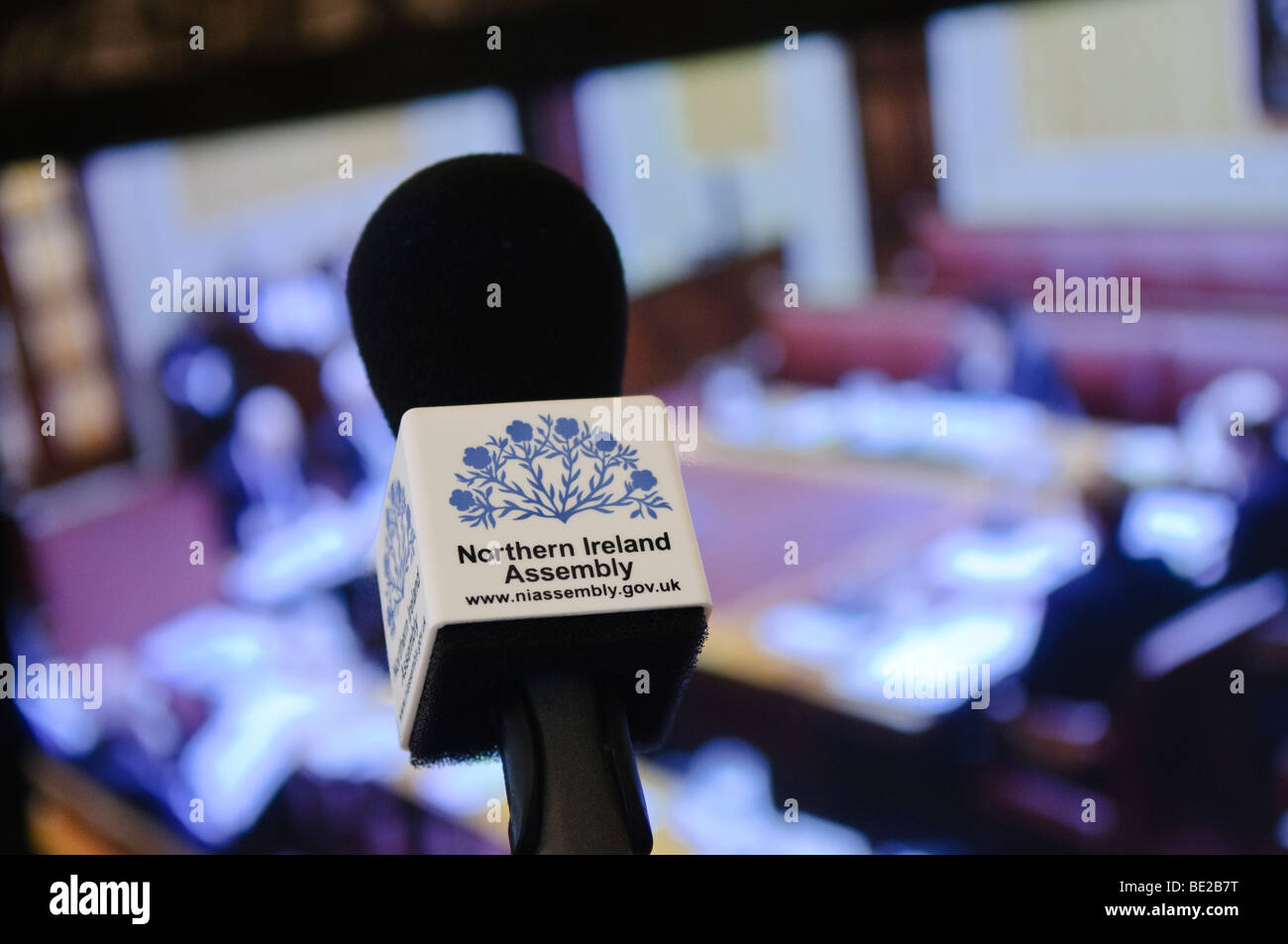 Microphone with 'Northern Ireland Assembly' in front of a Television screen, showing coverage from the executive chamber Stock Photo