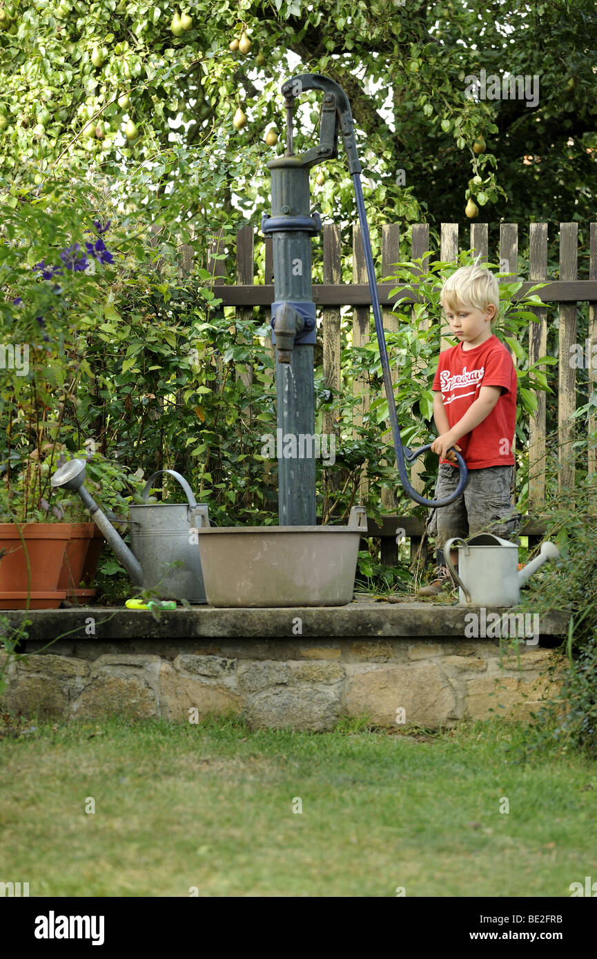 A Three Year Old Boy Plays With An Outdoor Vintage Hand Water Pump
