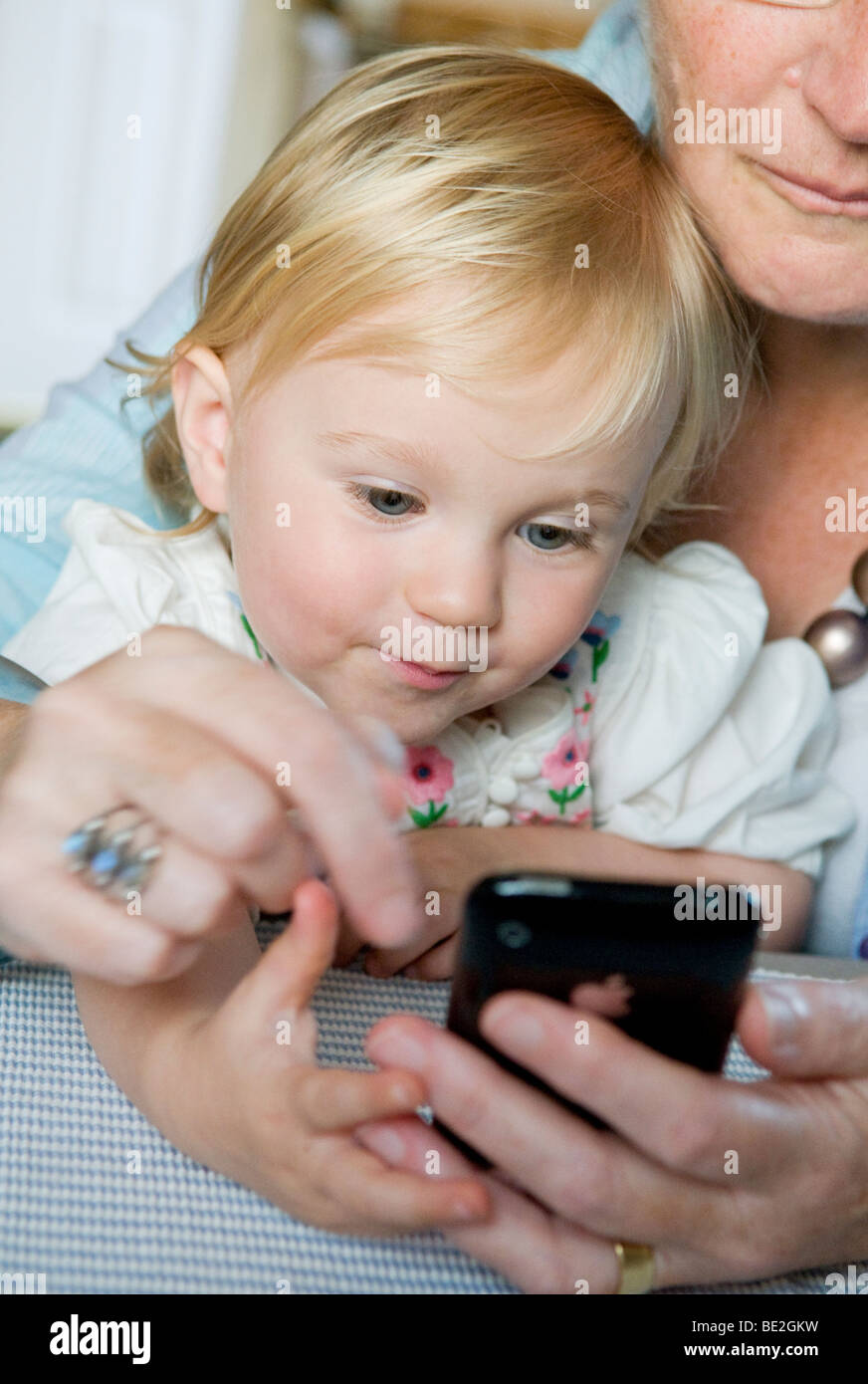 Baby girl, toddler, playing with an adult and their mobile phone, an iphone. Stock Photo