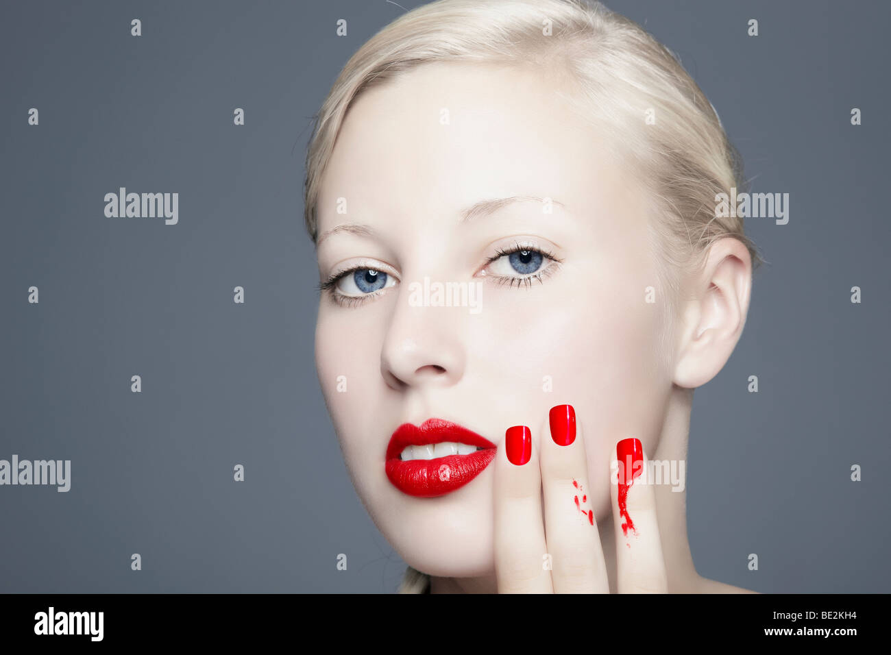 Portrait of a young blond woman with smeared nail polish looking towards the viewer, imperfect, beauty Stock Photo