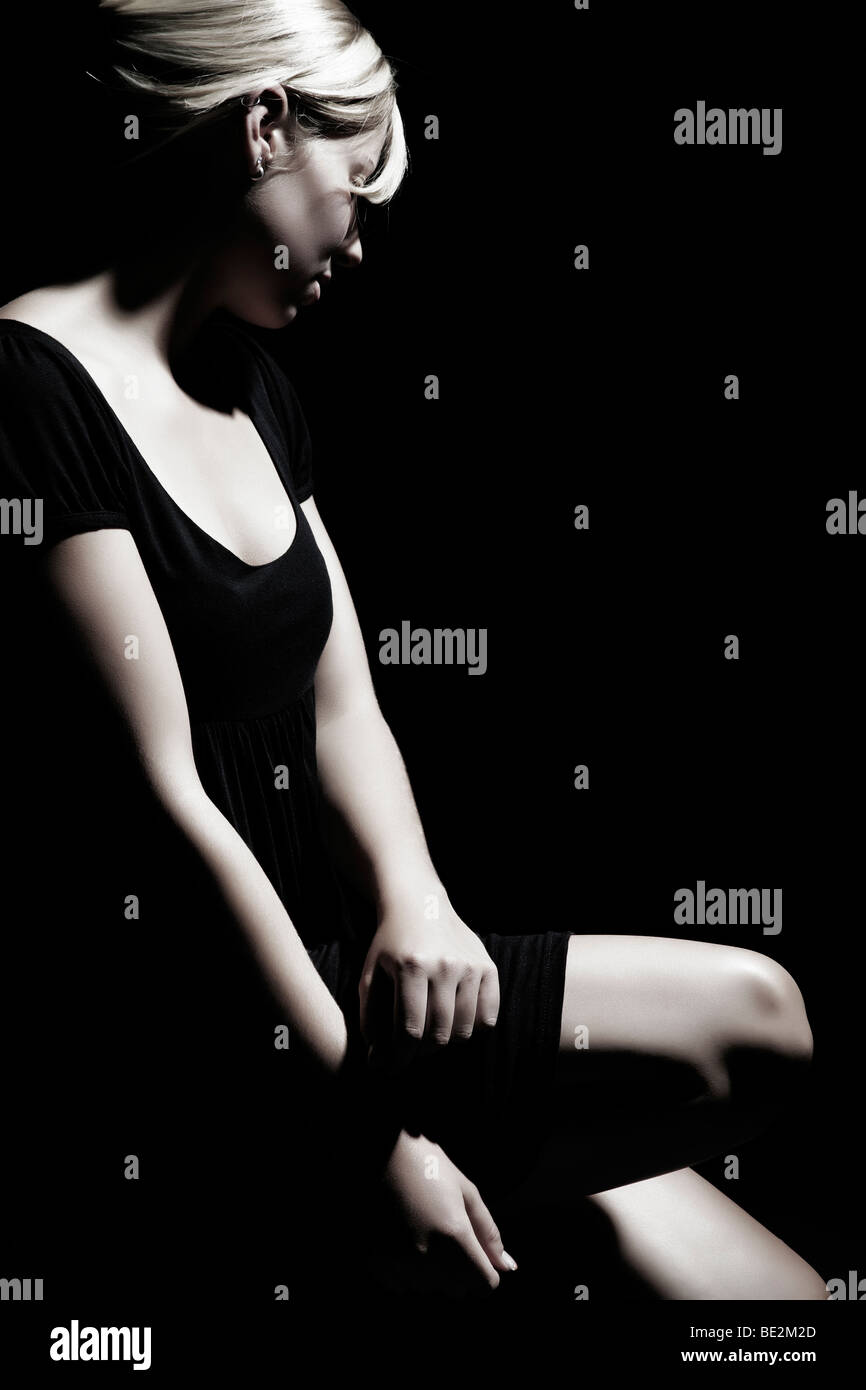 Portrait of a young woman wearing a black dress, kneeling with her gaze averted Stock Photo