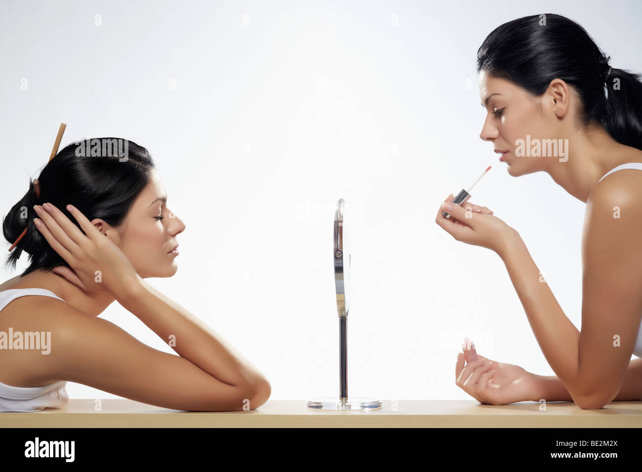 Two young women applying makeup sitting opposite one another, beauty Stock Photo