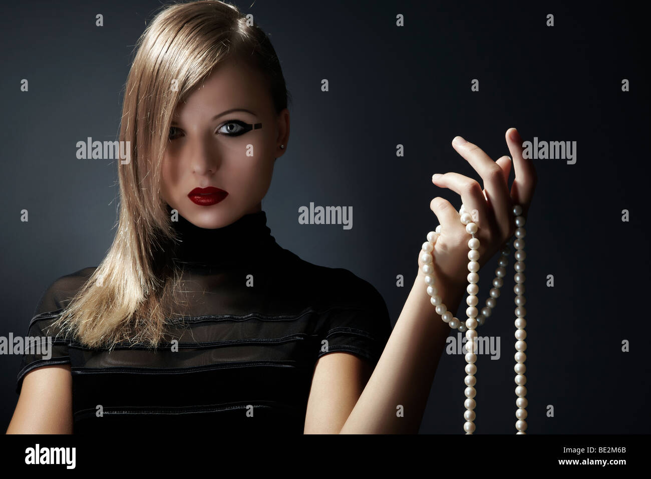 Young blond woman wearing a black dress holding a pearl necklace in her hand, fashion Stock Photo